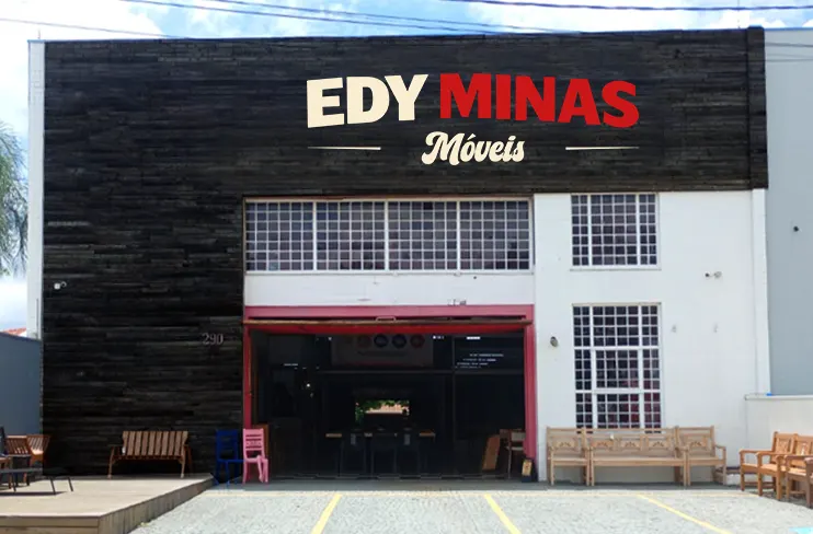 Fachada da Edy Minas Móveis: galpão de madeira escura com o letreiro da marca e bancos de madeira na calçada
